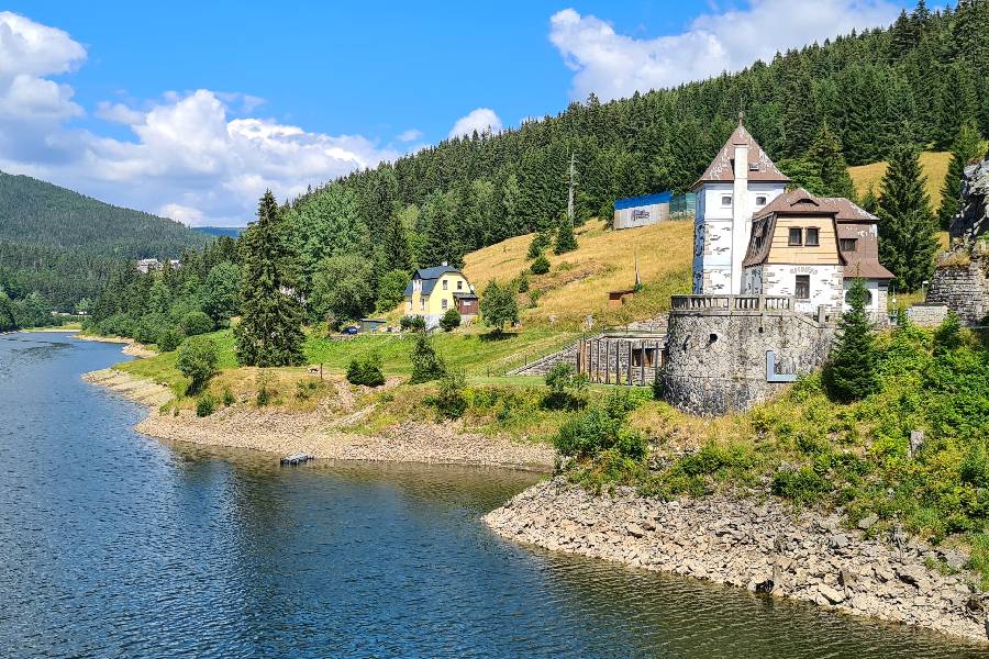 Лабская плотина и водохранилище с живописным зданием, окружённым лесистыми холмами.